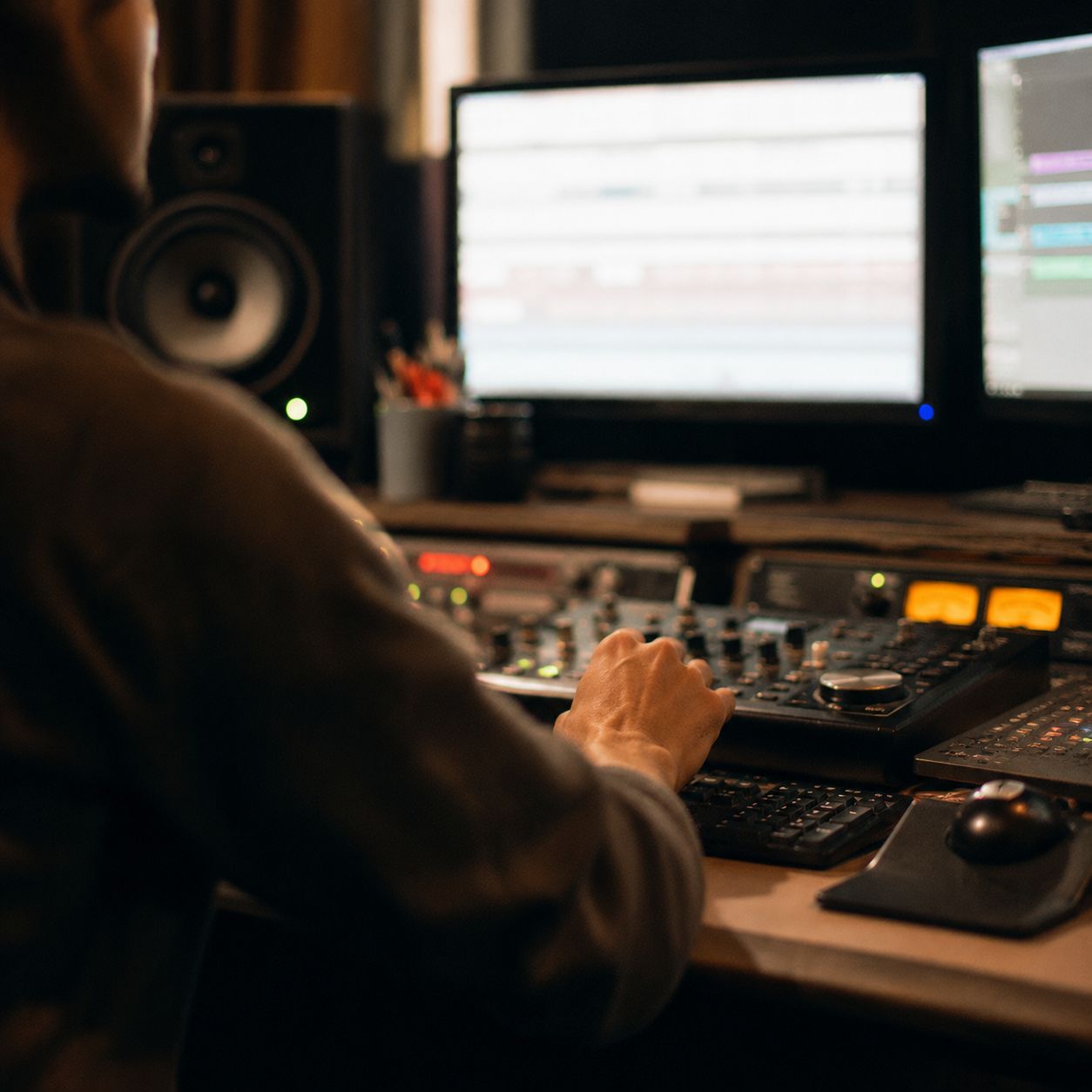 Hand adjusting a mixing console during audio post work with waveform displays on screen.