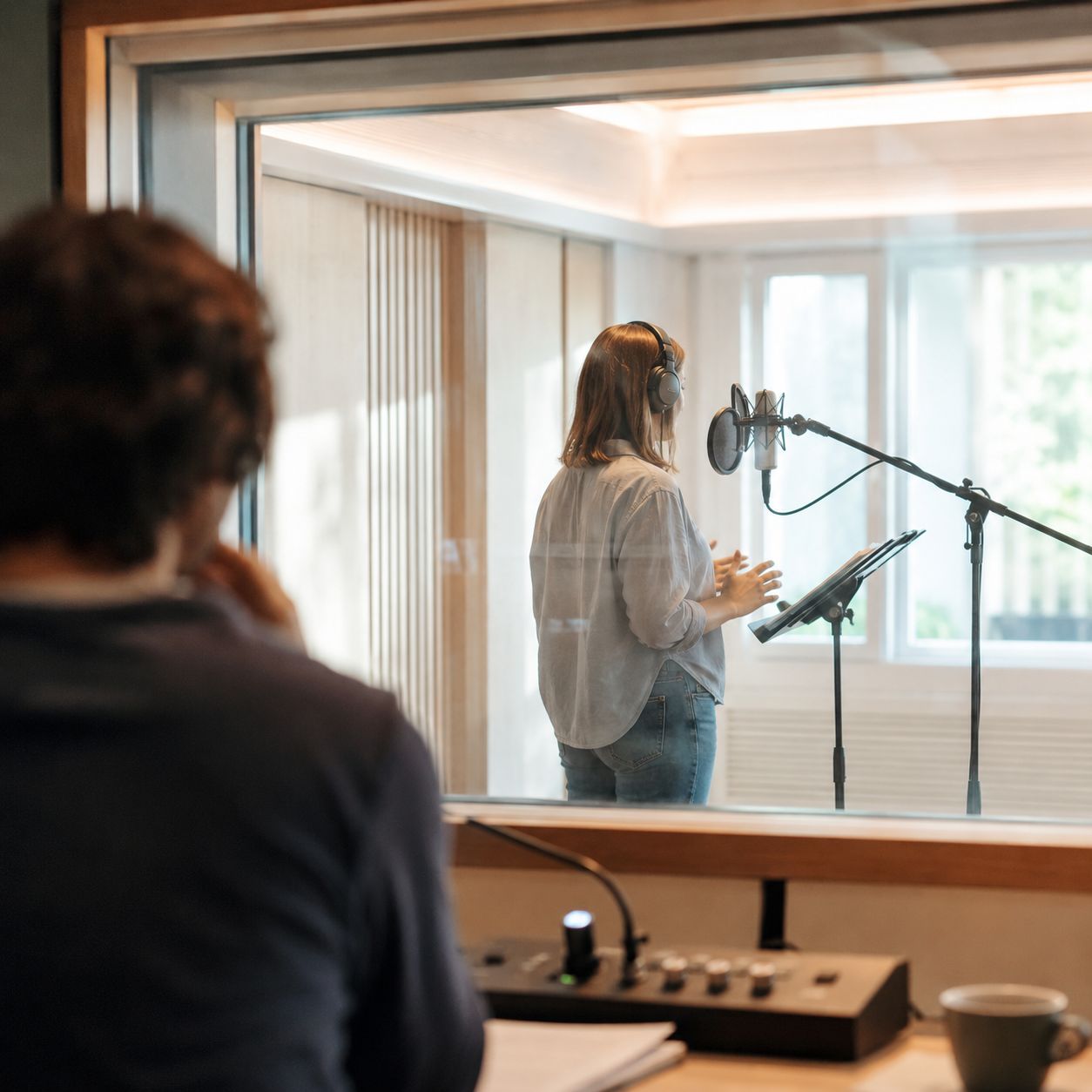 Voice performer in a booth during a directed session with a microphone and pop filter.